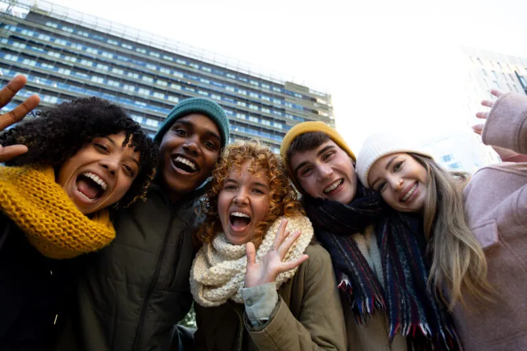 Group of happy multiracial friends looking at camera waving hand and keeping warm in winter time in the city